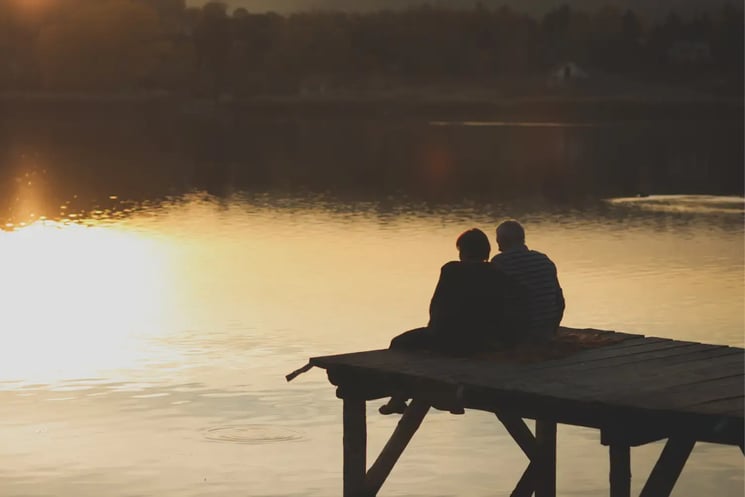 A man and woman on a jetty, watching the sunset