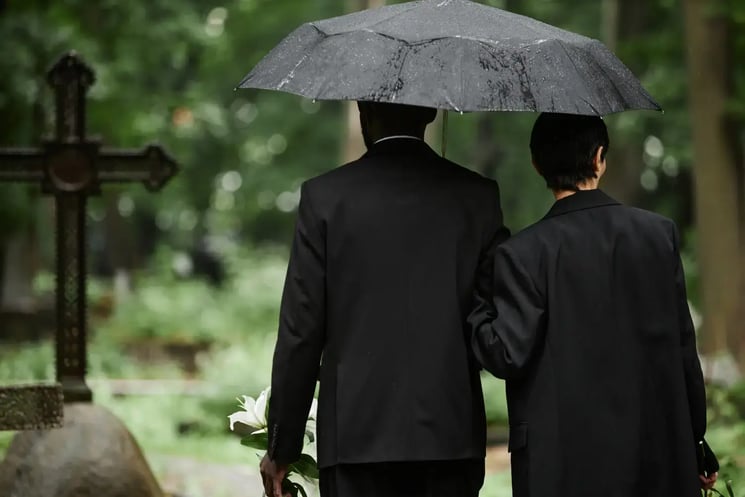 A man and woman dressed in back, under an umbrella seen from behind