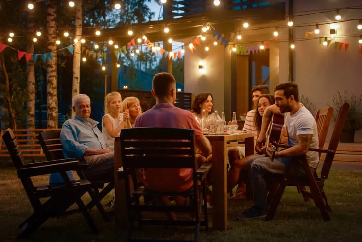 A group of people dining outdoors. A man plays guitar.