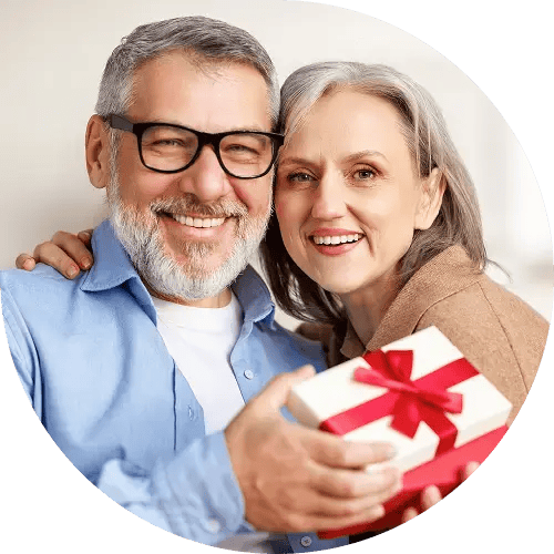 A man and woman smiling at the camera. The man is holding a present.