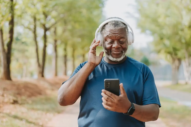 A man in a park, wearing headphones and looking at his phone
