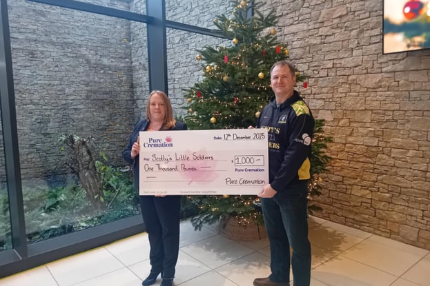 A man and woman in front of a Christmas tree, smiling at the camera, holding a big cheque