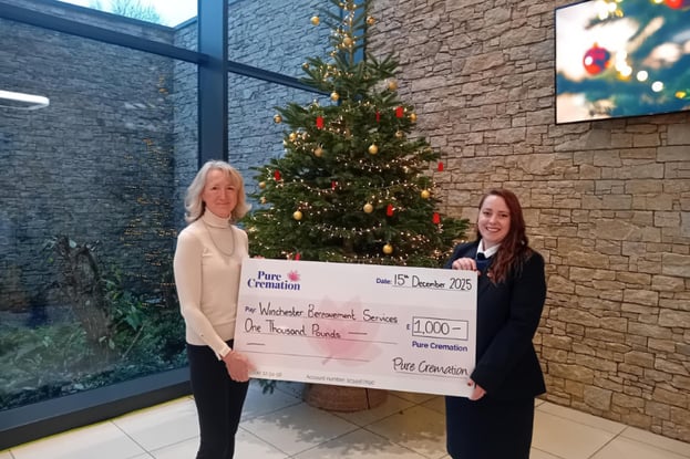 Two women smiling at the camera, holding a big cheque in front of a Christmas tree