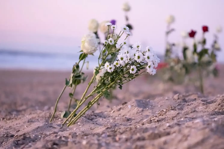 A bouquet of flowers stuck in the sand on a beach 