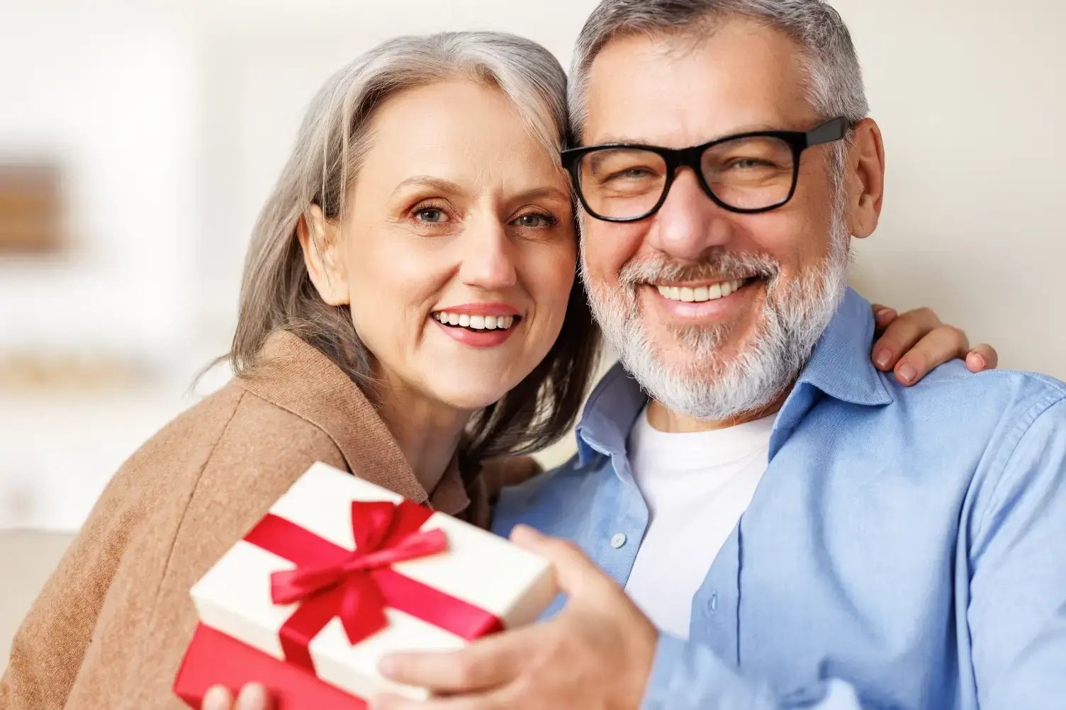 A man and woman smiling at the camera. The man is holding a present.