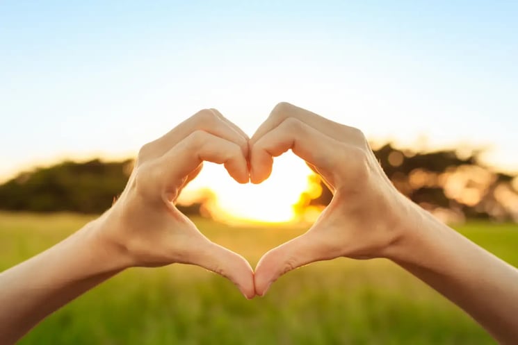 Two hands forming a heart in front of a sunset
