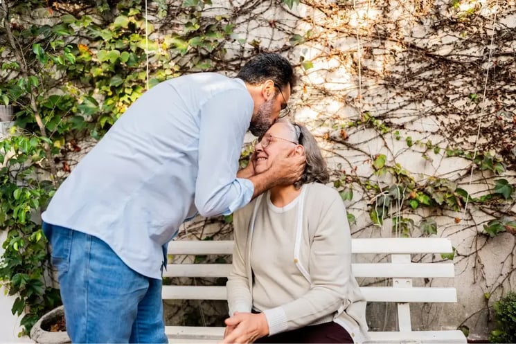 An adult son giving his mother a kiss on the head