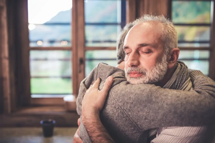 A man hugging someone, looking solemn 