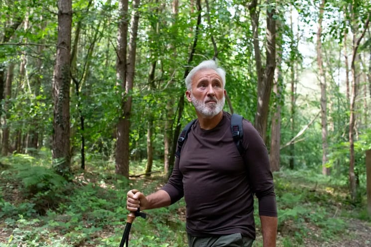 A man walking in the forest holding a stick