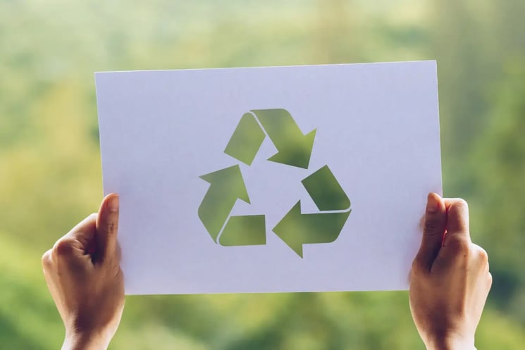 A piece of paper with a recycling symbol, being held up against a green background