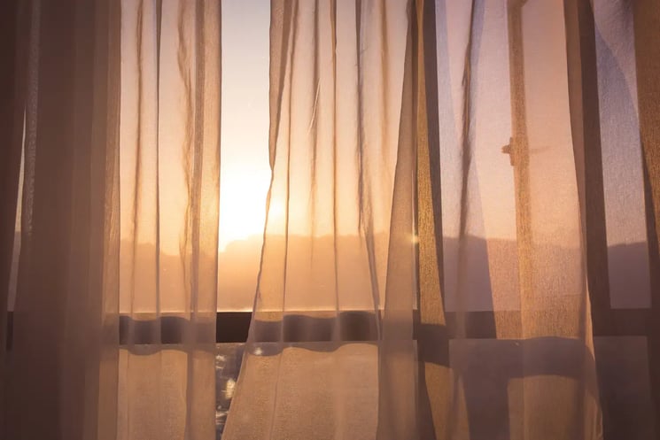 A sunset seen through a window with transparent curtains