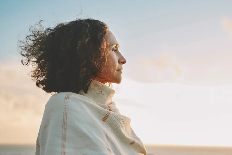 A woman standing on a beach, looking out at the sunset